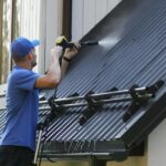 man standing on ladder and cleaning house metal roof with high pressure washer