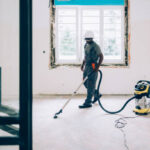 An African American construction worker vacuuming the floors while renovating an apartment.