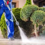 Caucasian Worker in His 30s with Pressure Washer Cleaning Residential Driveway. Garden and Home Surrounding Maintenance.