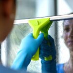 Woman washing windows at home, she is drying the glass surface with a squeegee